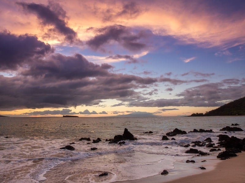 Purple sunset over rocks at Maluaka Beach in Makena, Maui